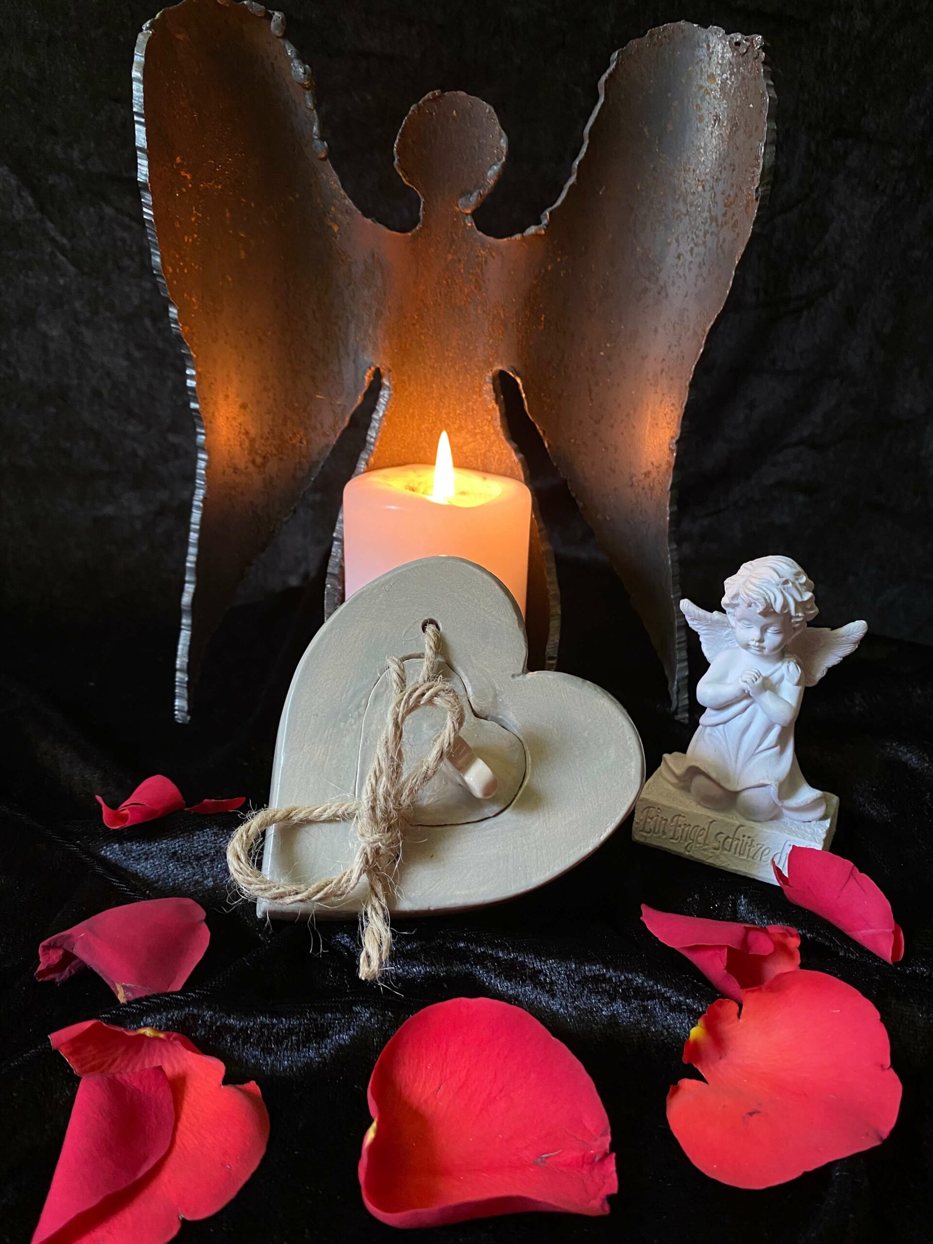 Engelsfigur hinter Kerze und Herzsymbol